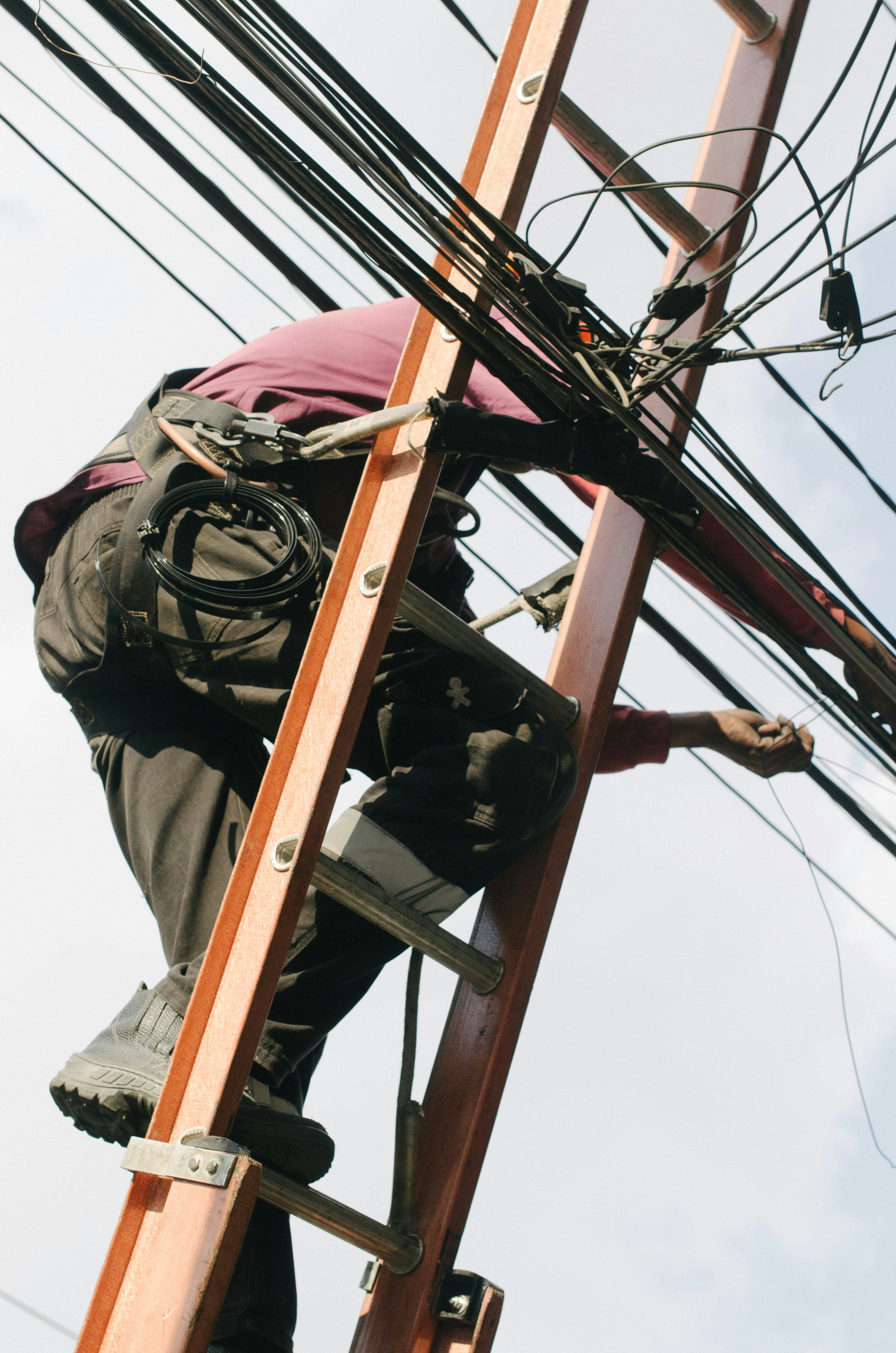 Electrician high on a ladder working on cables, unable to answer their phone